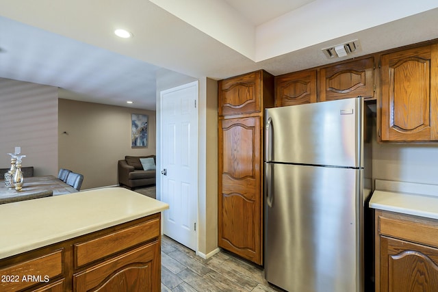 kitchen with visible vents, brown cabinetry, freestanding refrigerator, light countertops, and wood finish floors