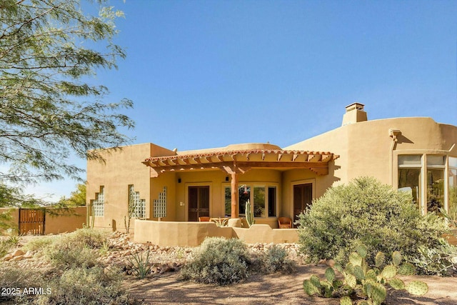 back of house with a chimney, fence, and stucco siding