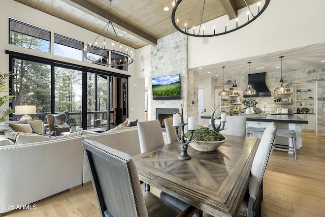 dining space featuring wood ceiling, beam ceiling, a fireplace, a chandelier, and light wood-type flooring