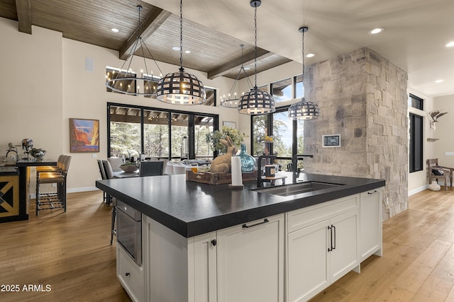 kitchen with white cabinetry, hanging light fixtures, a center island, stainless steel microwave, and light wood-type flooring