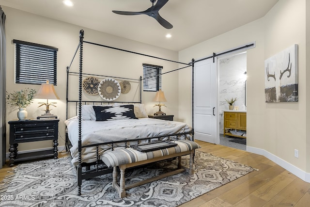 bedroom with hardwood / wood-style floors, a barn door, ceiling fan, and ensuite bathroom