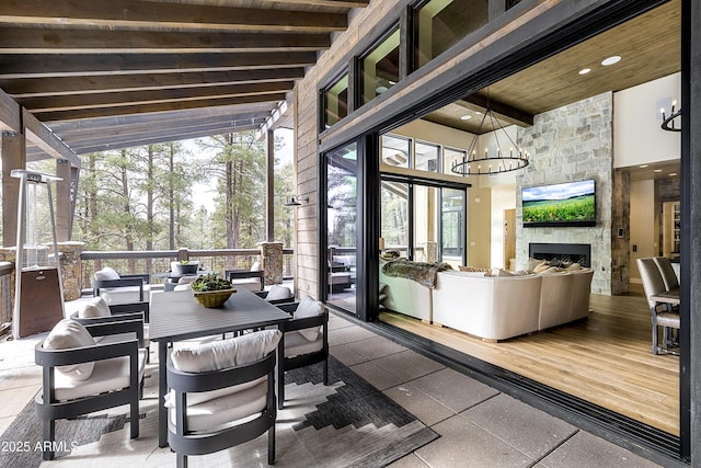 sunroom / solarium featuring a notable chandelier, beam ceiling, a stone fireplace, and wooden ceiling