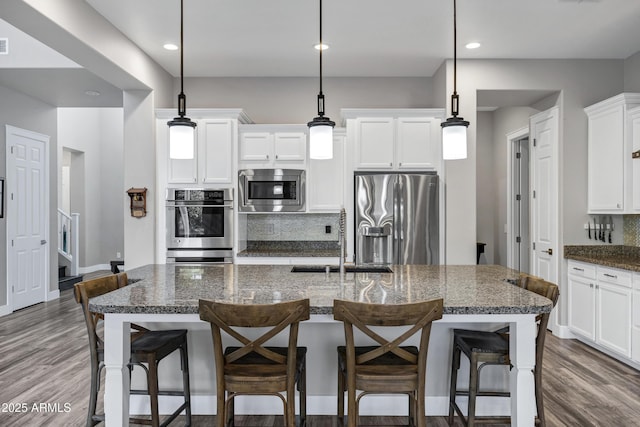 kitchen with decorative light fixtures, dark stone counters, an island with sink, and appliances with stainless steel finishes