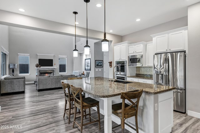 kitchen featuring appliances with stainless steel finishes, an island with sink, white cabinets, a kitchen bar, and dark stone counters