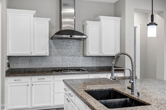 kitchen featuring wall chimney range hood, sink, and dark stone counters