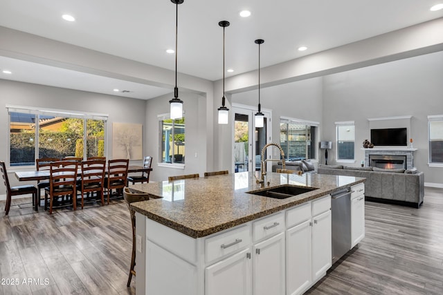 kitchen with sink, white cabinetry, hanging light fixtures, a center island with sink, and dark stone countertops