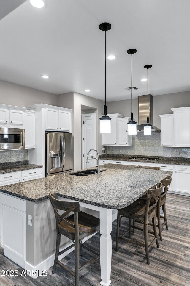 kitchen with appliances with stainless steel finishes, pendant lighting, sink, a large island, and wall chimney range hood