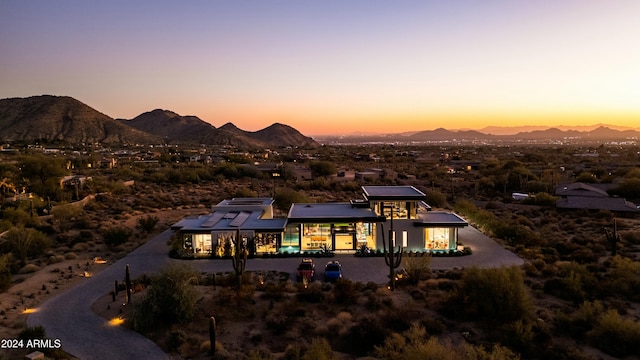 back of house at dusk with a mountain view and roof mounted solar panels