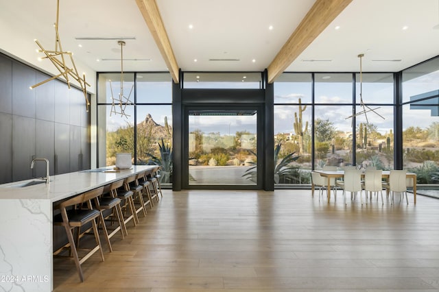 interior space with dark wood-style floors, an inviting chandelier, a sink, a wall of windows, and beamed ceiling