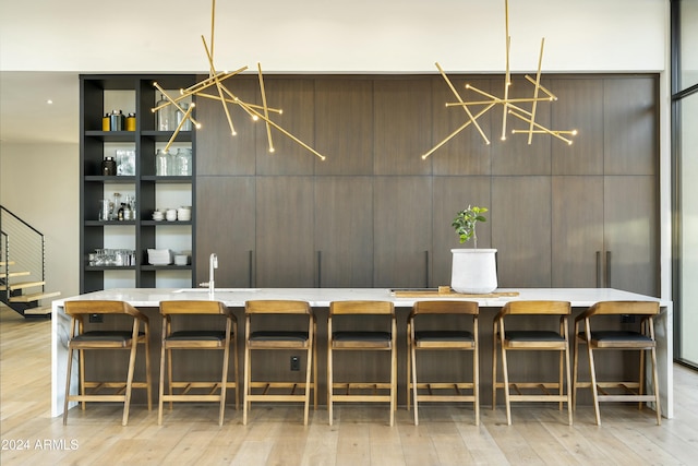 bar featuring a chandelier, light wood-style floors, stairway, and a sink