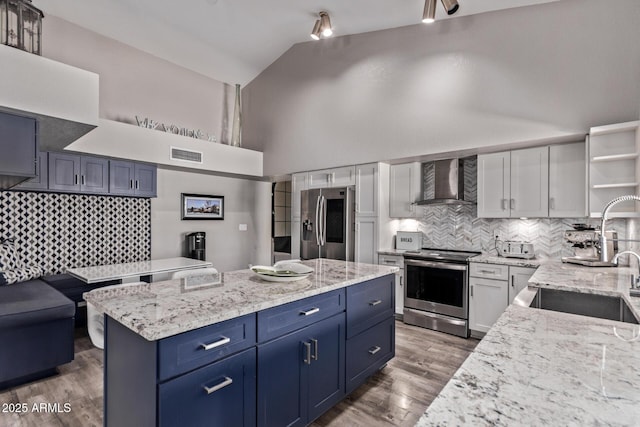 kitchen with a sink, blue cabinets, stainless steel appliances, backsplash, and wall chimney exhaust hood