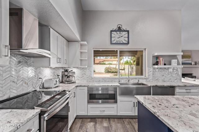 kitchen with wall chimney exhaust hood, light stone counters, open shelves, and stainless steel electric range