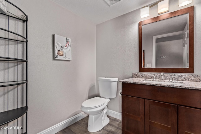 bathroom featuring wood finished floors, vanity, baseboards, toilet, and visible vents