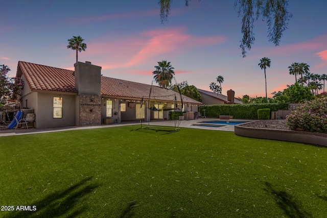 back of property at dusk with a chimney, a tile roof, a patio, and a lawn