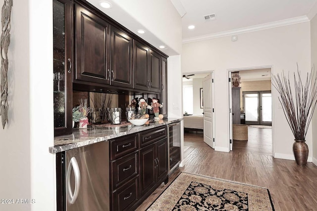 bar with light stone counters, dark brown cabinetry, ornamental molding, and dark wood-type flooring