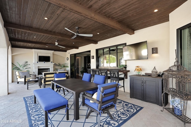 dining area featuring ceiling fan, beam ceiling, wood ceiling, and an outdoor fireplace