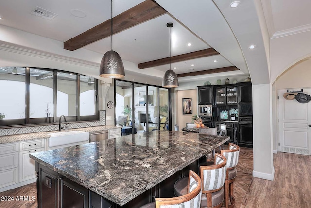 kitchen with decorative backsplash, sink, dark stone countertops, white cabinets, and a large island