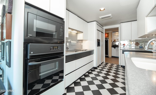 kitchen with visible vents, black appliances, white cabinetry, dark floors, and light countertops