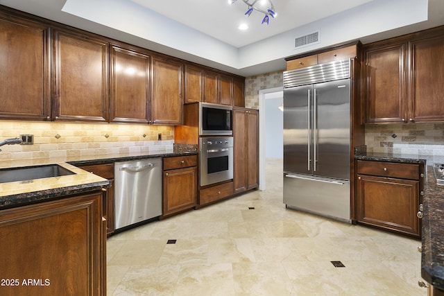 kitchen featuring backsplash, dark stone counters, sink, and built in appliances