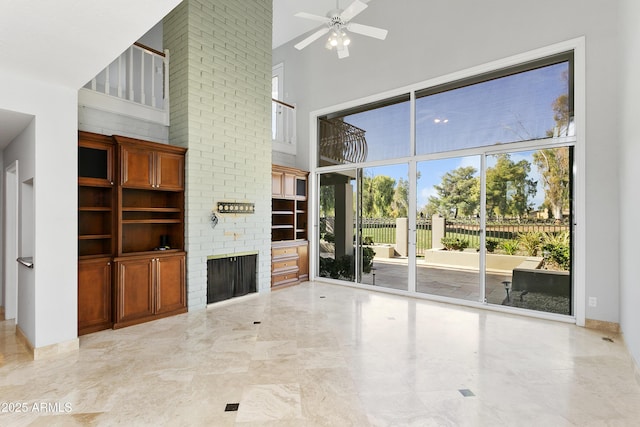 unfurnished living room with a brick fireplace, a high ceiling, and ceiling fan