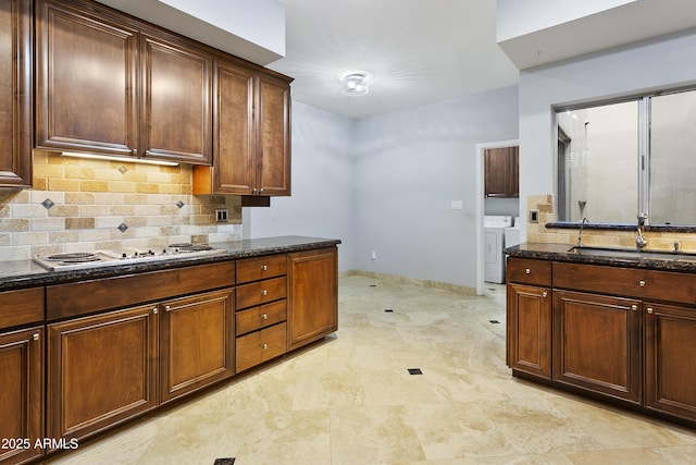 kitchen with washer and dryer, decorative backsplash, sink, white electric stovetop, and dark stone counters