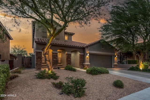 mediterranean / spanish-style home featuring fence, an attached garage, stucco siding, stone siding, and a tile roof