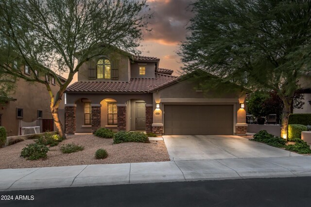 mediterranean / spanish home with stucco siding, stone siding, concrete driveway, a garage, and a tiled roof