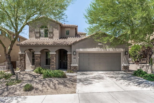 mediterranean / spanish-style house with stucco siding, driveway, a tile roof, stone siding, and a garage