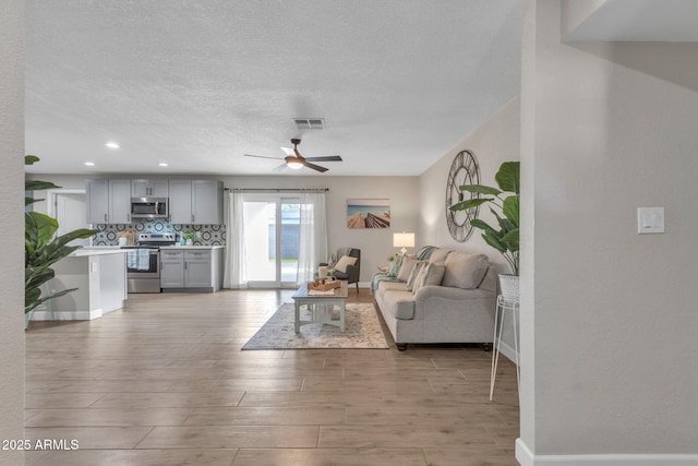 living room with ceiling fan, a textured ceiling, and light hardwood / wood-style floors