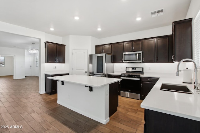 kitchen featuring sink, stainless steel appliances, a kitchen island, a kitchen breakfast bar, and dark brown cabinetry