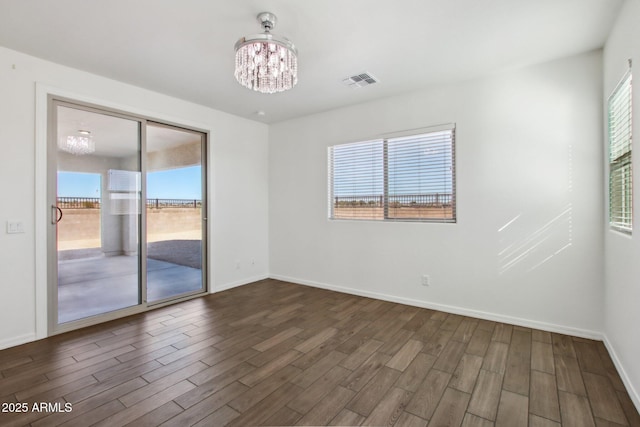 empty room featuring a chandelier, plenty of natural light, and dark hardwood / wood-style floors