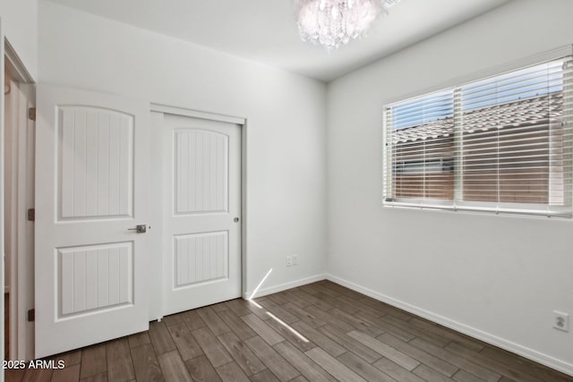 unfurnished bedroom featuring a notable chandelier, hardwood / wood-style floors, and a closet