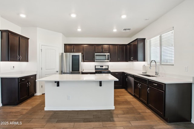 kitchen featuring a kitchen breakfast bar, stainless steel appliances, a kitchen island, dark brown cabinetry, and sink