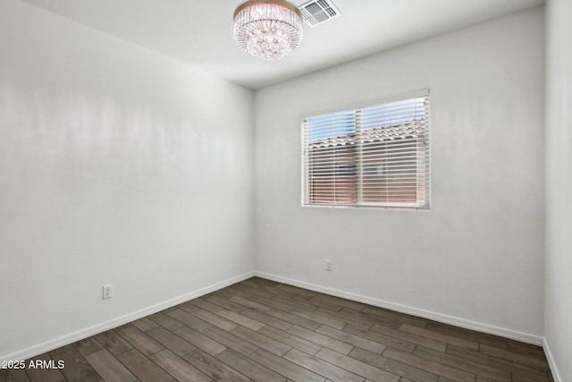 empty room with dark hardwood / wood-style flooring and an inviting chandelier