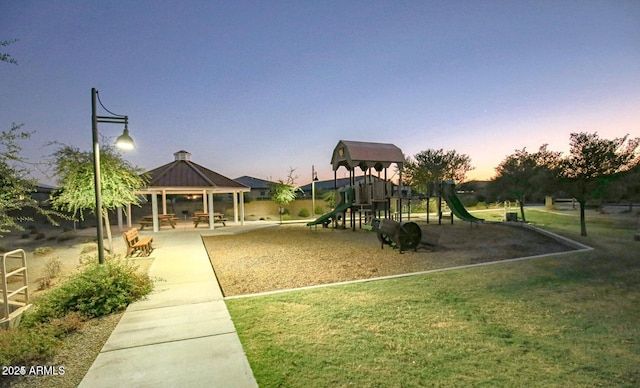 playground at dusk featuring a lawn and a gazebo