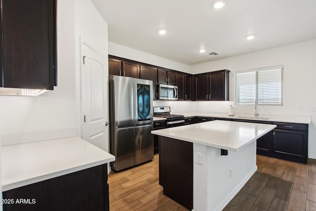 kitchen with a kitchen breakfast bar, stainless steel appliances, a kitchen island, sink, and dark brown cabinets