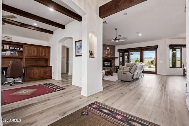 interior space featuring beamed ceiling, ceiling fan, a large fireplace, and light wood-type flooring