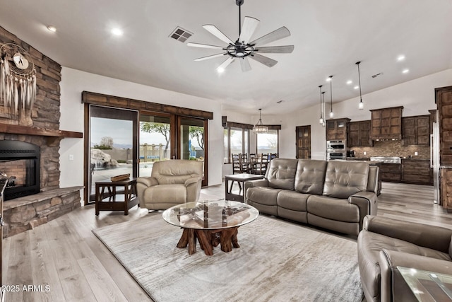 living room with ceiling fan, vaulted ceiling, a fireplace, and light hardwood / wood-style flooring