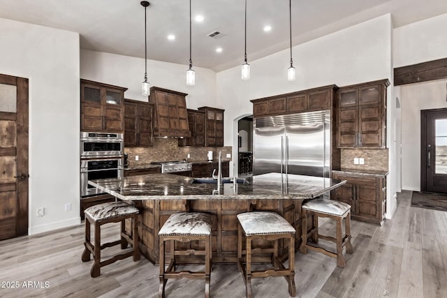 kitchen featuring sink, a large island with sink, dark stone countertops, decorative light fixtures, and appliances with stainless steel finishes