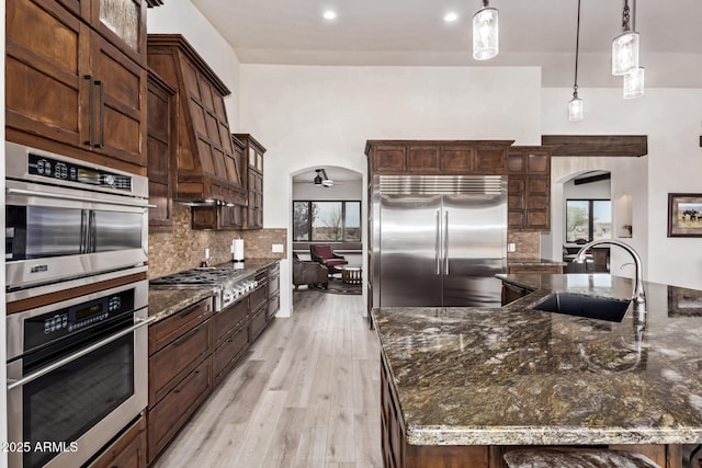 kitchen with dark stone counters, sink, decorative light fixtures, dark brown cabinets, and stainless steel appliances