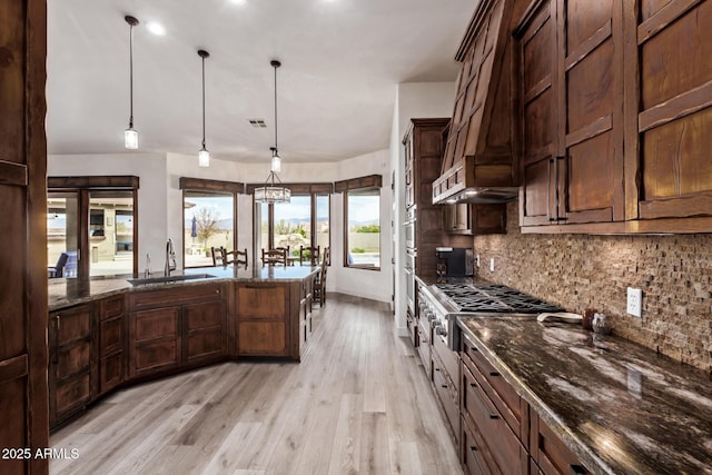 kitchen featuring decorative backsplash, dark stone countertops, sink, and hanging light fixtures