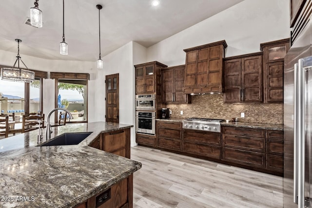 kitchen featuring pendant lighting, dark stone counters, sink, decorative backsplash, and appliances with stainless steel finishes