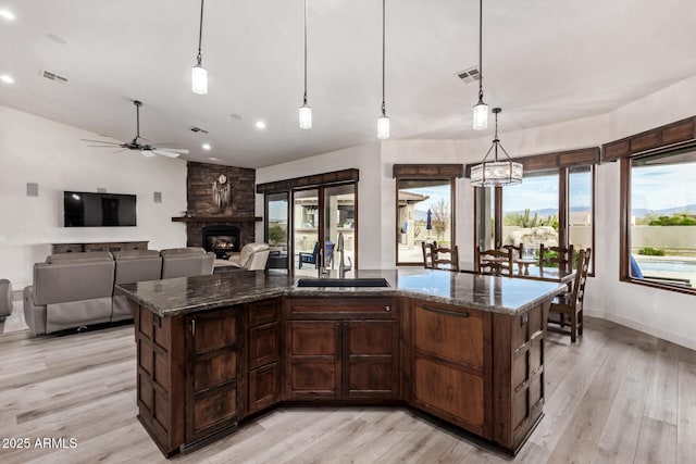 kitchen with dark stone countertops, sink, hanging light fixtures, and a kitchen island with sink