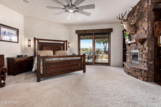 carpeted bedroom with access to outside, a stone fireplace, and ceiling fan