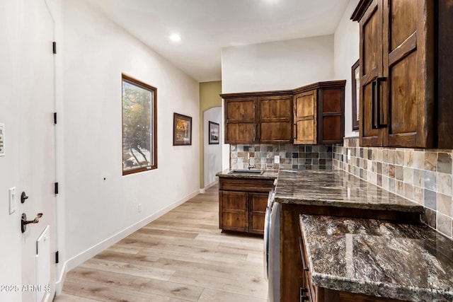 kitchen with dark stone counters, decorative backsplash, dark brown cabinets, and light hardwood / wood-style floors