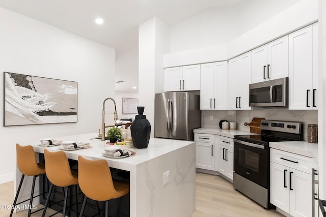 kitchen featuring light wood finished floors, a center island with sink, a kitchen bar, white cabinets, and stainless steel appliances