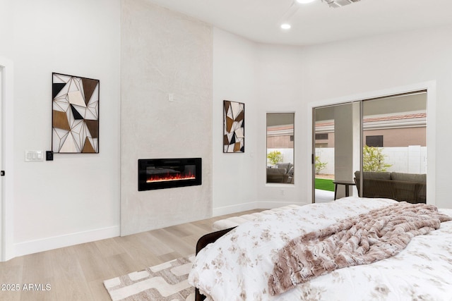 bedroom featuring baseboards, recessed lighting, a fireplace, a towering ceiling, and wood finished floors