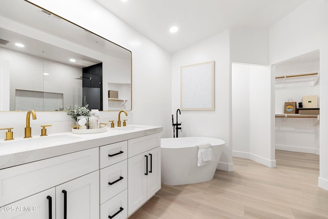 bathroom featuring double vanity, wood finished floors, a walk in shower, and a sink