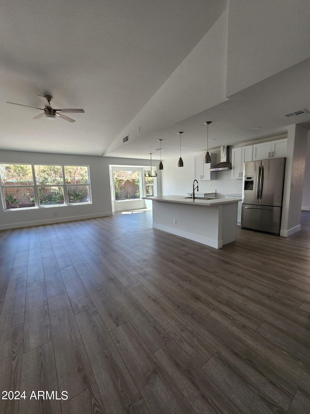 kitchen with white cabinets, stainless steel refrigerator with ice dispenser, decorative light fixtures, wall chimney range hood, and a kitchen island with sink