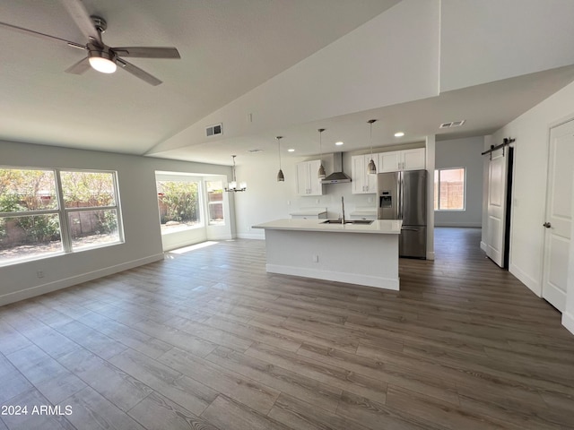 kitchen with stainless steel fridge, hanging light fixtures, wall chimney exhaust hood, white cabinetry, and a barn door